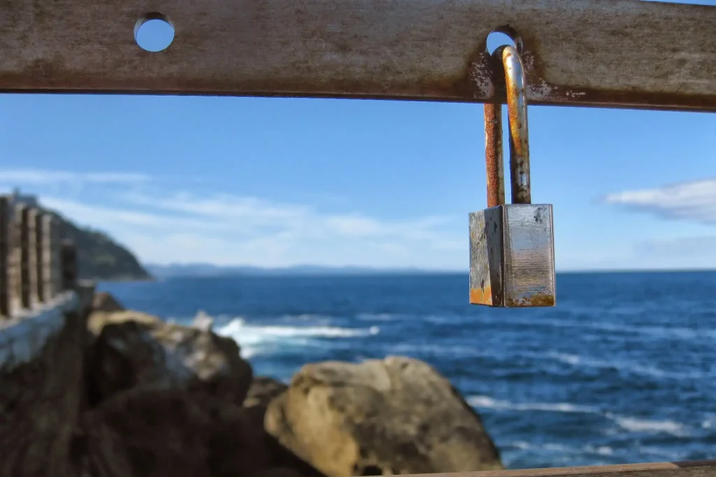 Padlock hanging from a bar in front of the sea