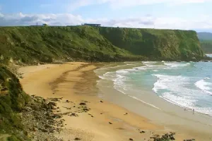 Playa de Los Locos sandy beach with steep hill behind and cliffs at the end.