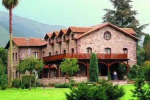 the hotel - a large reddish building red tiles and hills behind and a garden in front